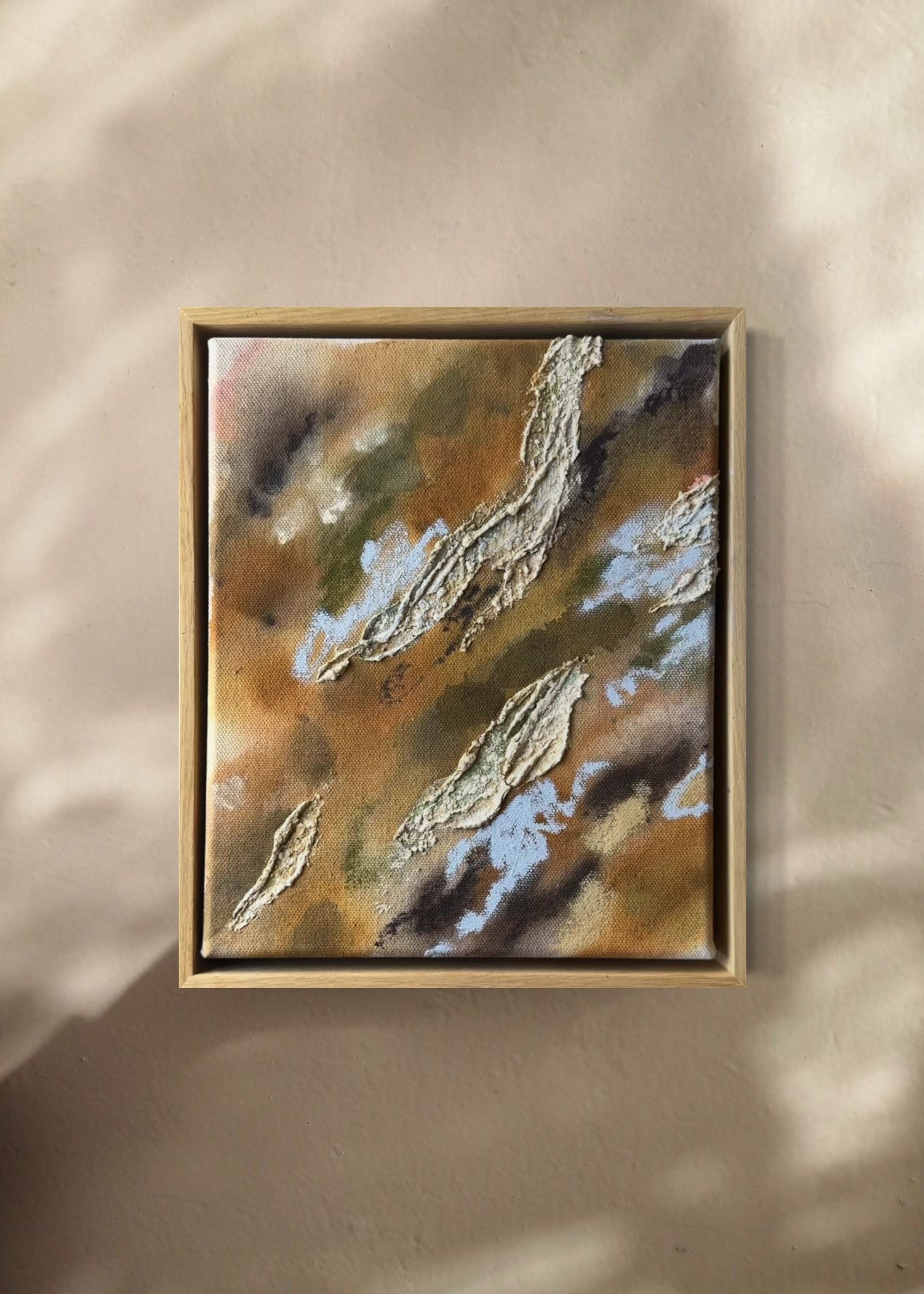 Abstract painting with textured, layered elements in shades of brown, green, and blue. The canvas features irregular shapes resembling organic forms. Framed in oak wood.