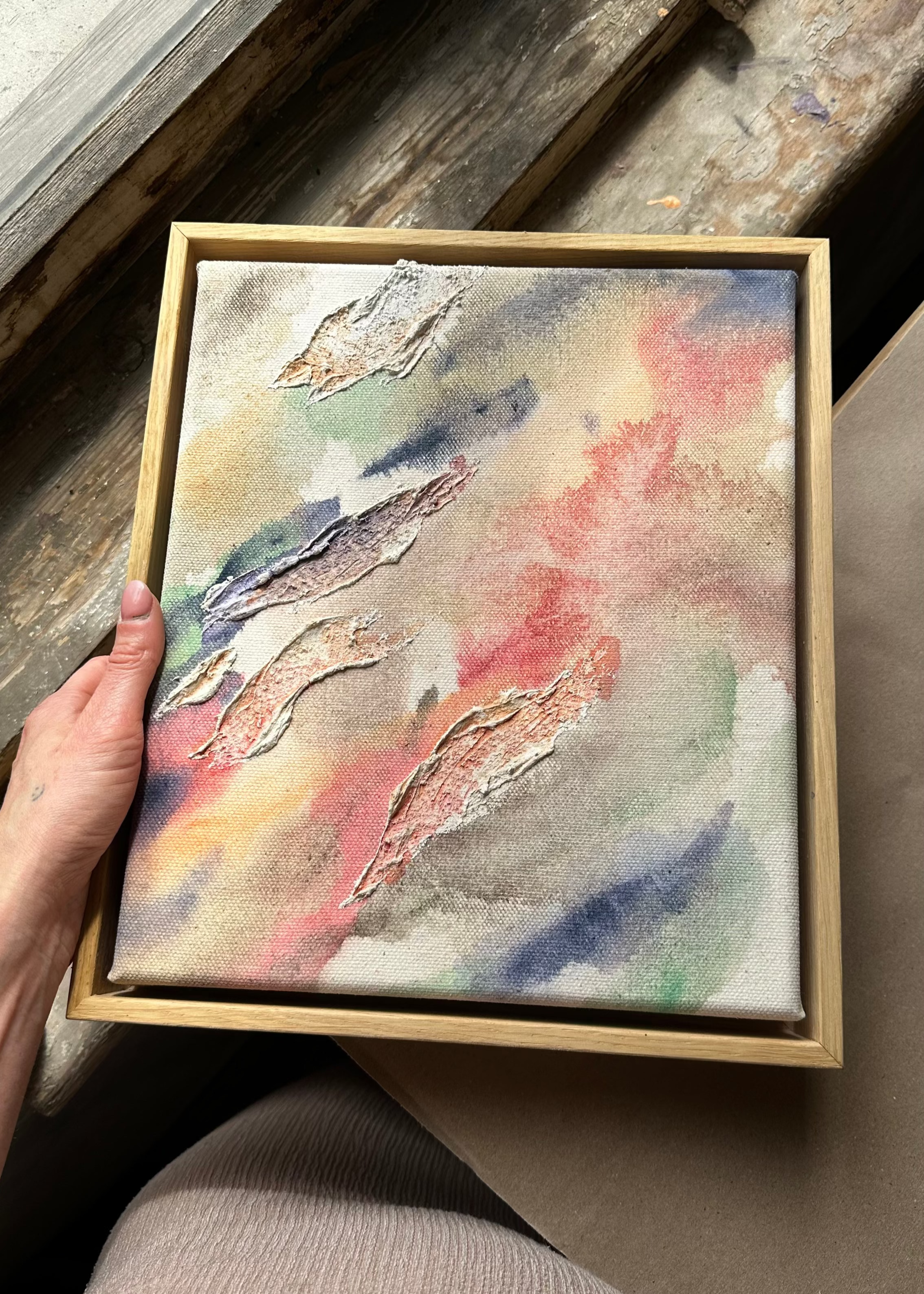Abstract painting highlighted through organic shaped textures. Featuring colors of beige, pink, green, dark purple and deep blue on a canvas background. Framed in an oak wood frame.