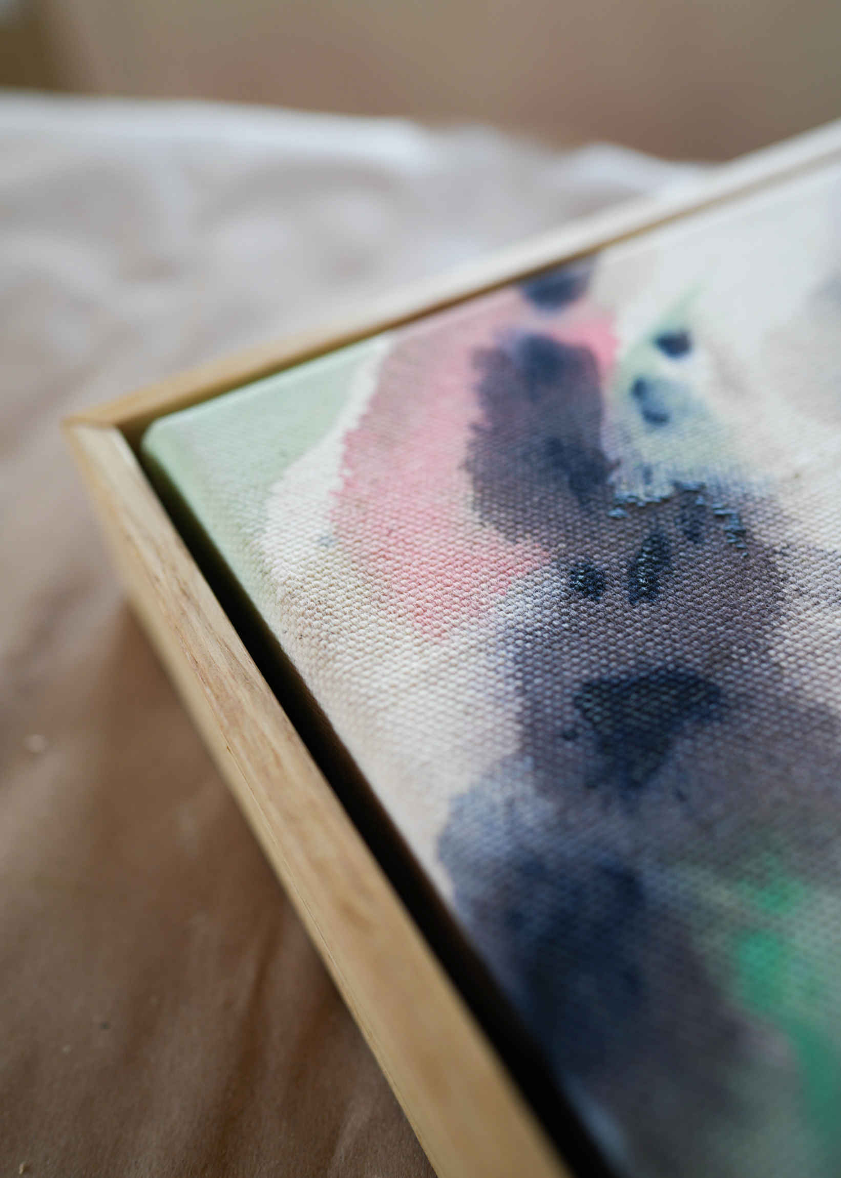 Abstract acrylic painting in a wooden frame displays blended swirls of pink, blue, and earthy tones on textured cotton canvas, evoking a serene mood.