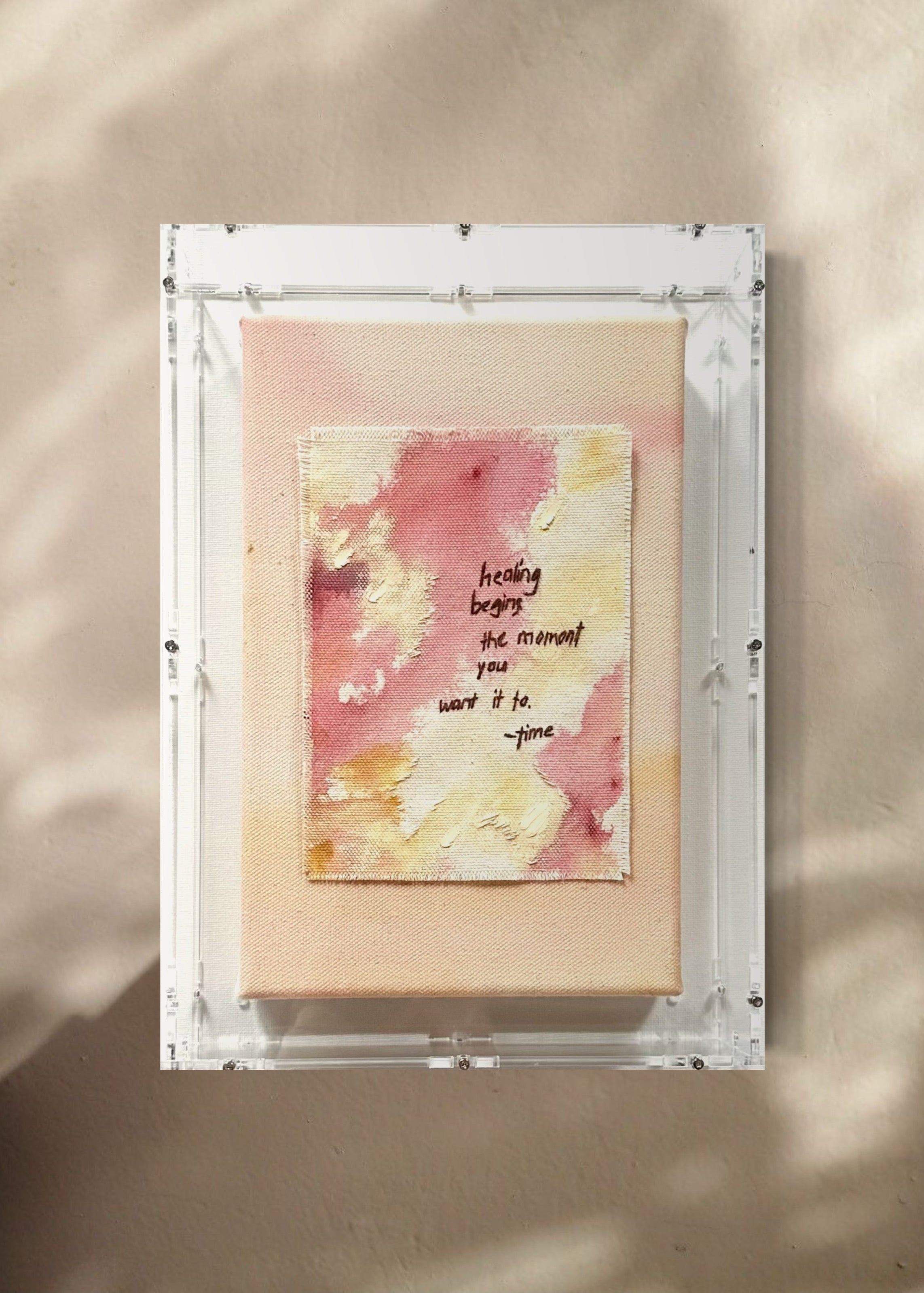 The abstract painting features a soft pink, beige, and orange watercolor background. It has a hand-stitched poem that says, "Healing begins the moment you want it to." This artwork radiates hope and is beautifully framed in clear acrylic.