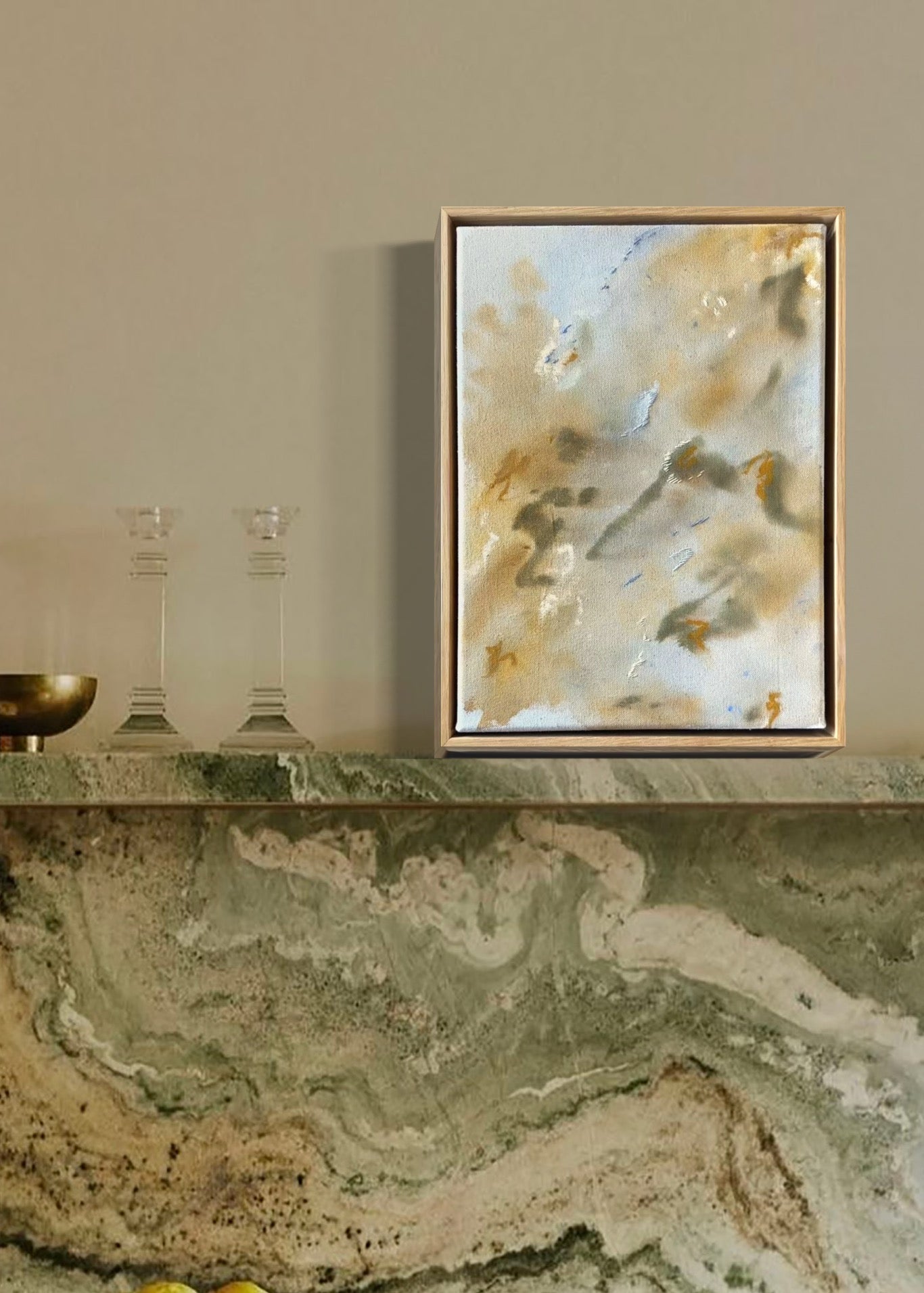Abstract painting featuring soft, blended colors in beige, brown, and hints of blue. The artwork has a textured, stitched surface and is framed in a light oak wood frame.