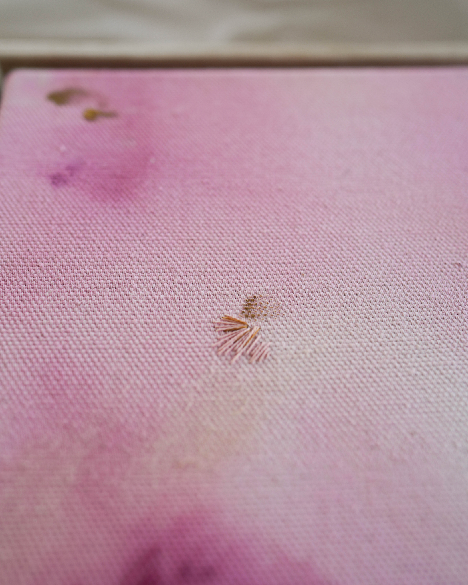 Abstract painting with soft pink, purple, and orange colors blending together. It has gold and dark purple embroidery details on a canvas. The painting is framed in light wood.