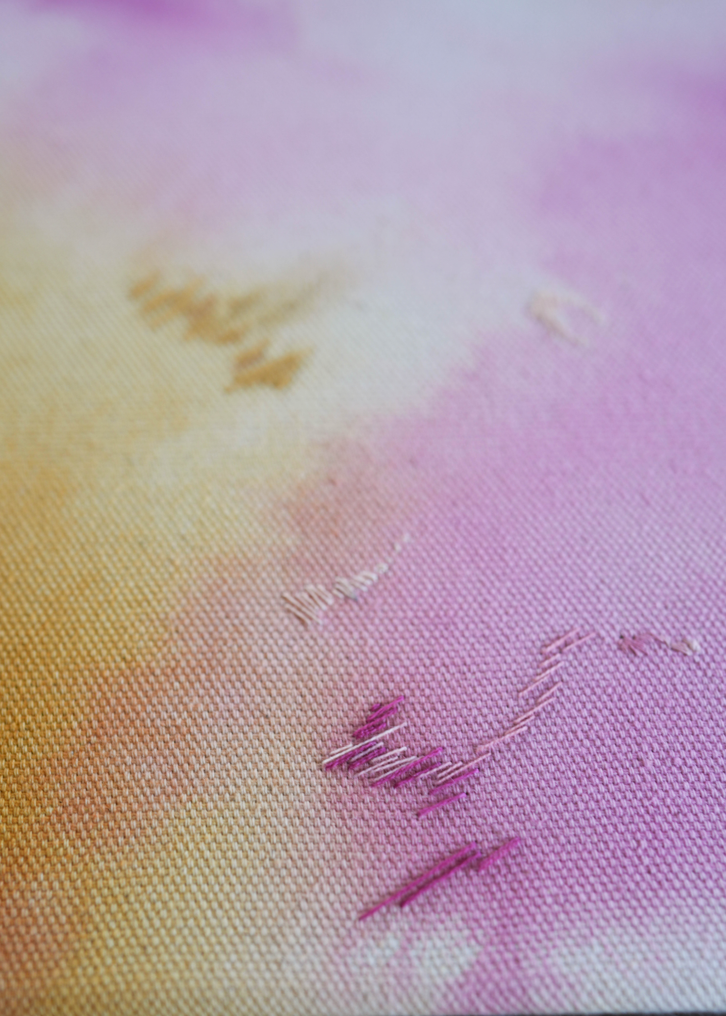 Abstract painting with soft pink, purple, and orange colors blending together. It has gold and dark purple embroidery details on a canvas. The painting is framed in light wood.
