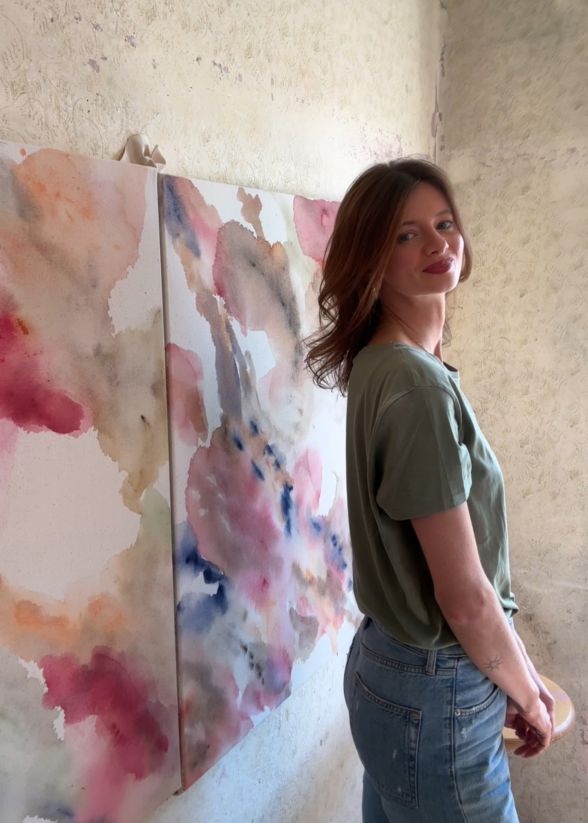 The artist Christina Anna Sperber standing in her studio space in front of two large scale abstract pieces.