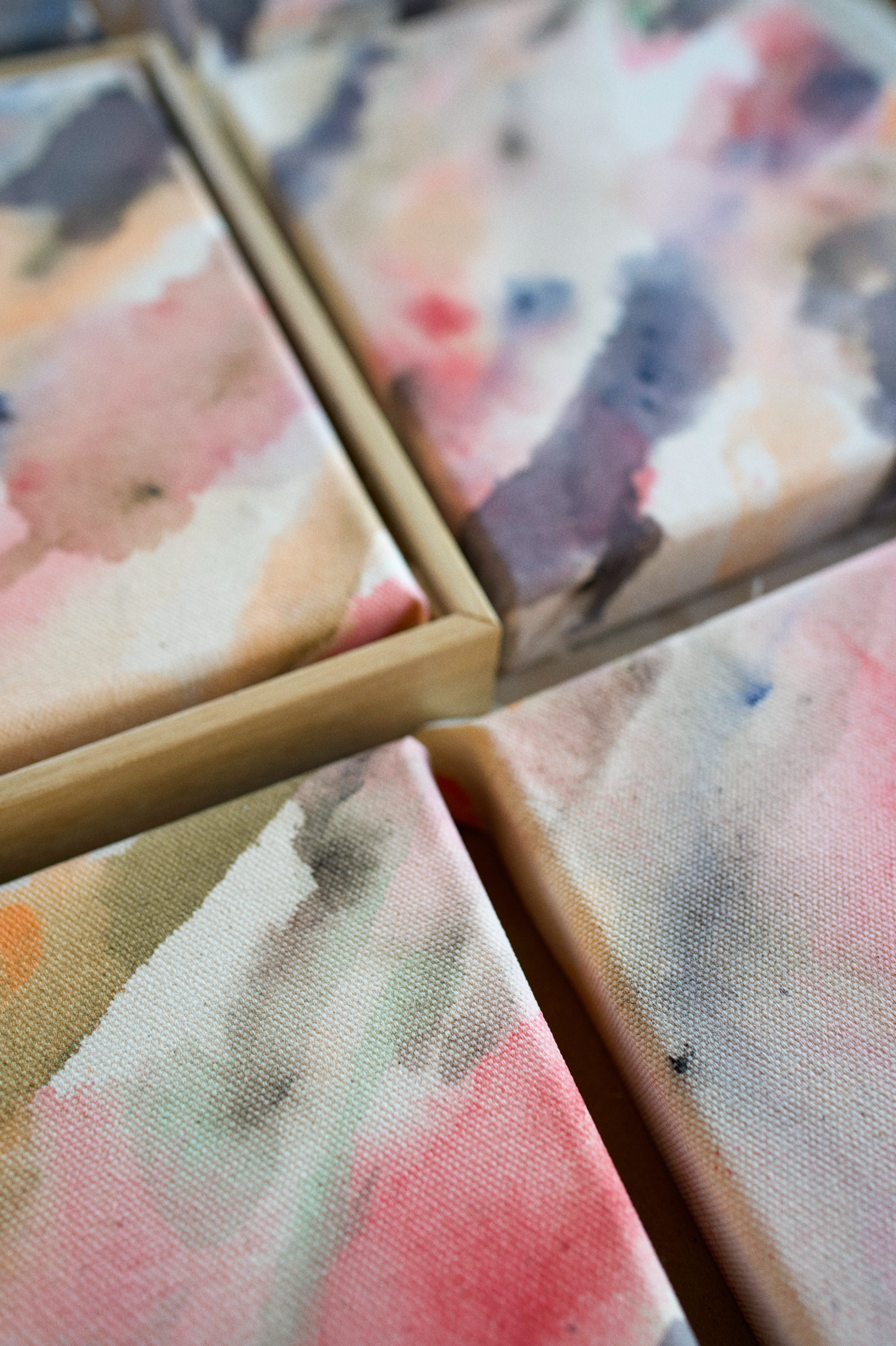 Multiple colorful, abstract fine art paintings laying next to each other on a table.