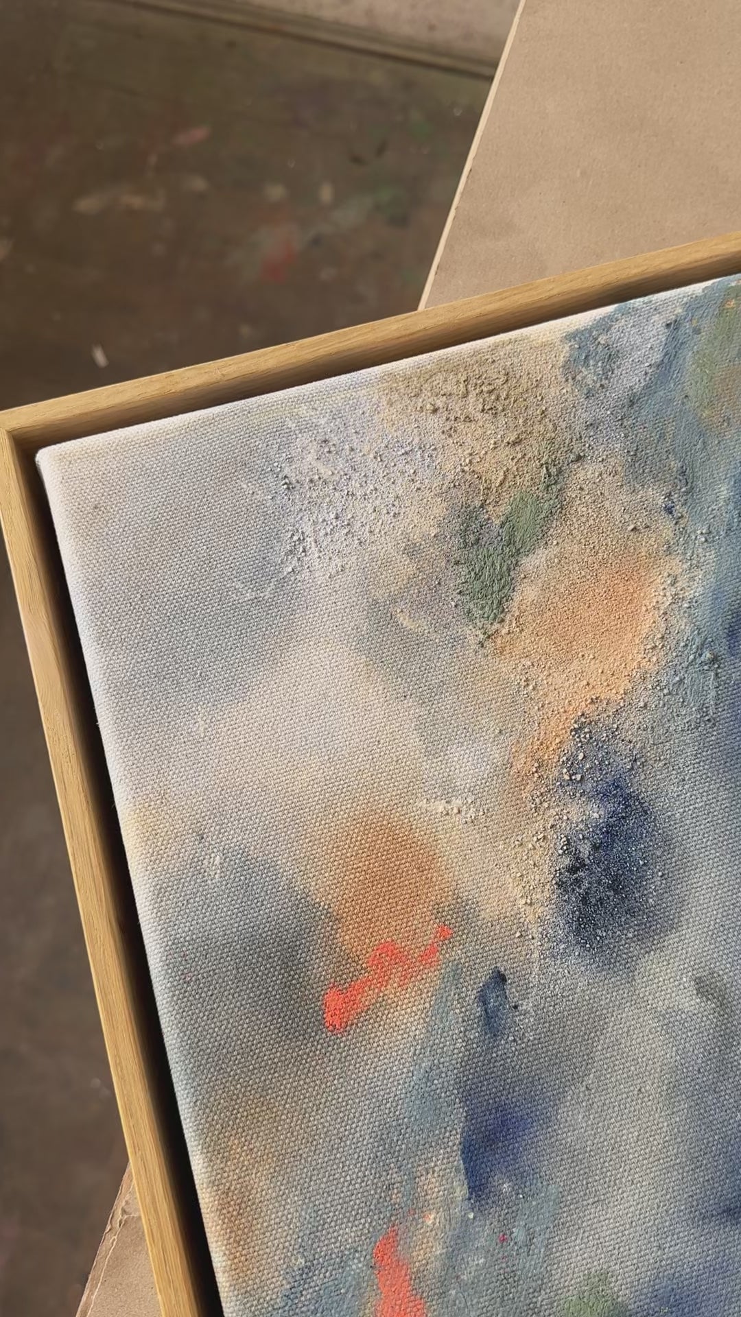 Abstract painting with swirling patterns in shades of blue, gray, green and orange, framed in oak wood.