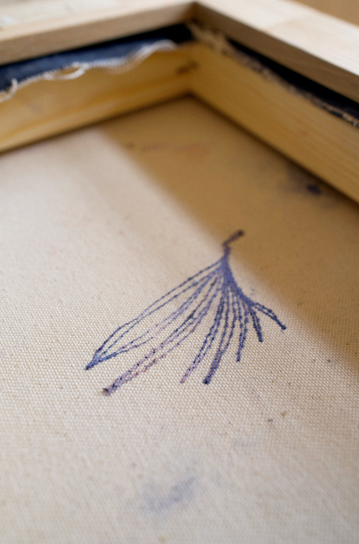 Backside stitching of an abstract painting with swirling blue and pink tones, framed in wood, evoking motion and emotion.