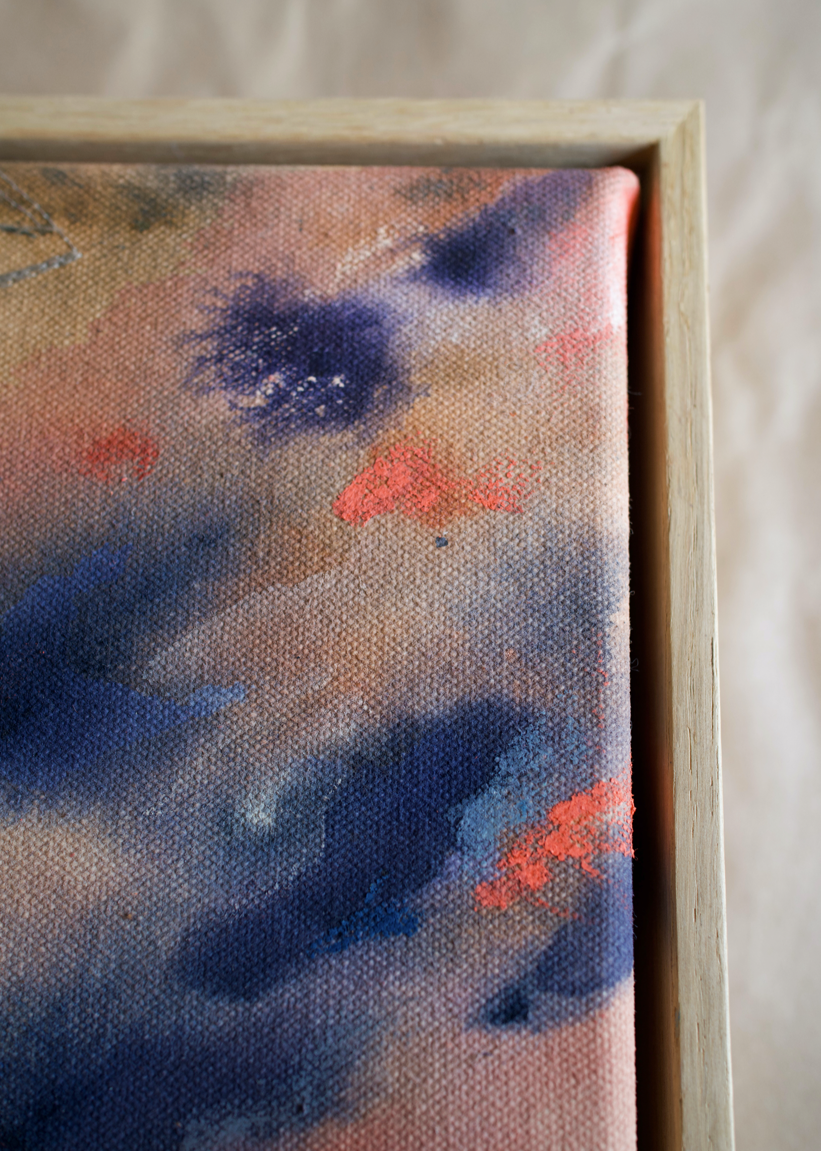 Detail shot of an abstract painting with swirling blue and pink tones, framed in wood, evoking motion and emotion.
