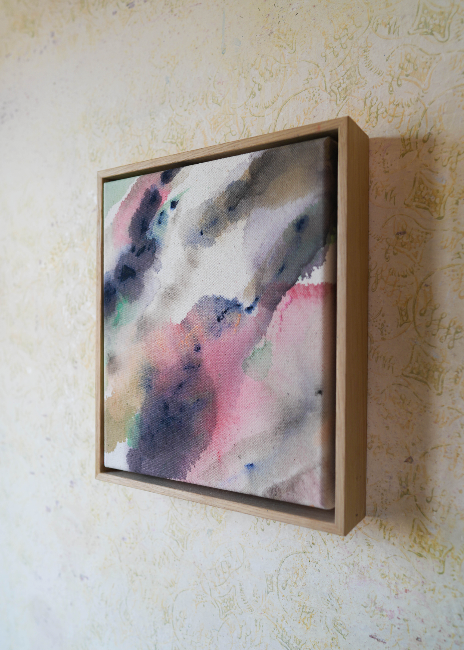 Abstract acrylic painting in a wooden frame displays blended swirls of pink, blue, and earthy tones on textured cotton canvas, evoking a serene mood.
