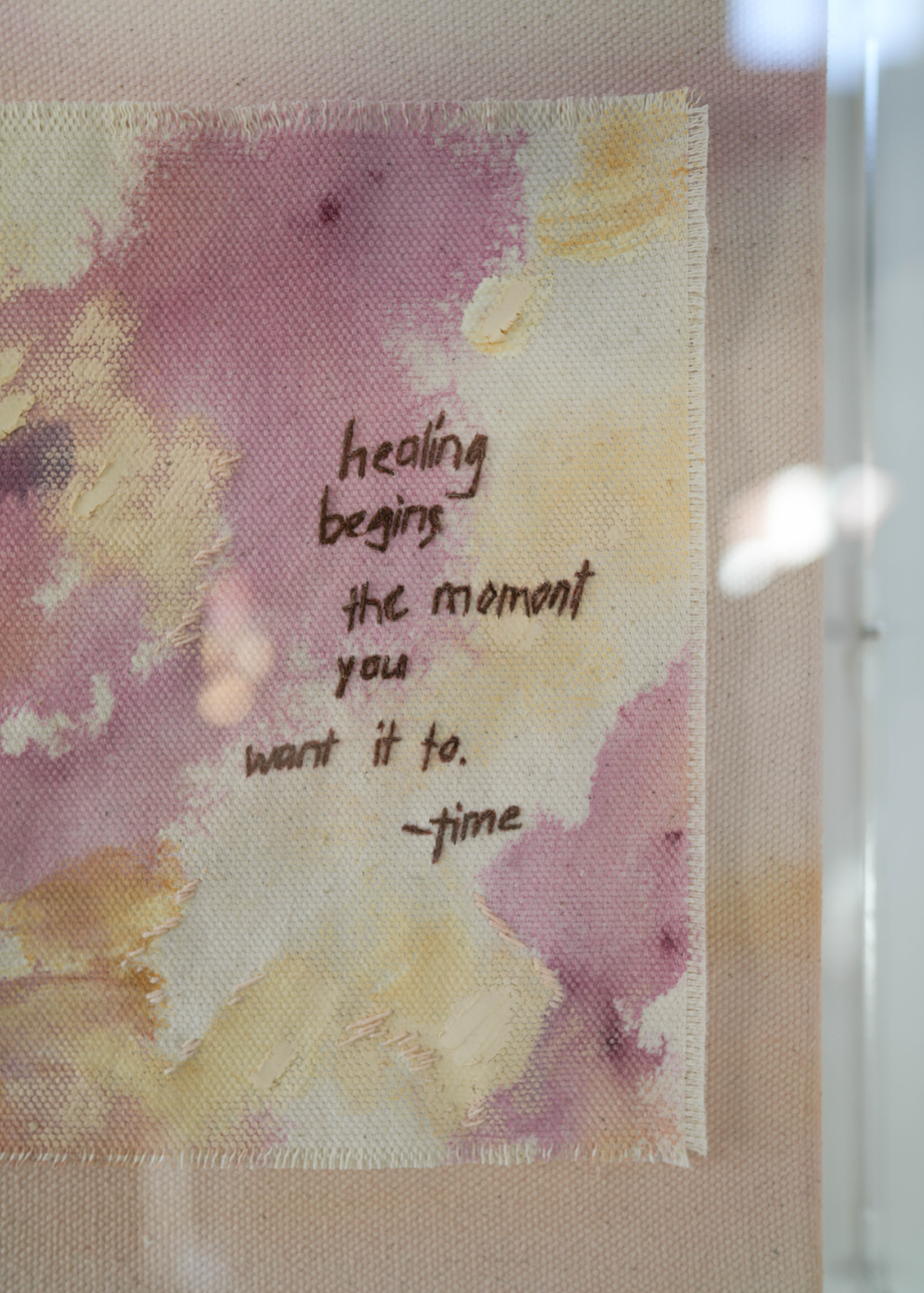 The abstract painting features a soft pink, beige, and orange watercolor background. It has a hand-stitched poem that says, "Healing begins the moment you want it to." This artwork radiates hope and is beautifully framed in clear acrylic.
