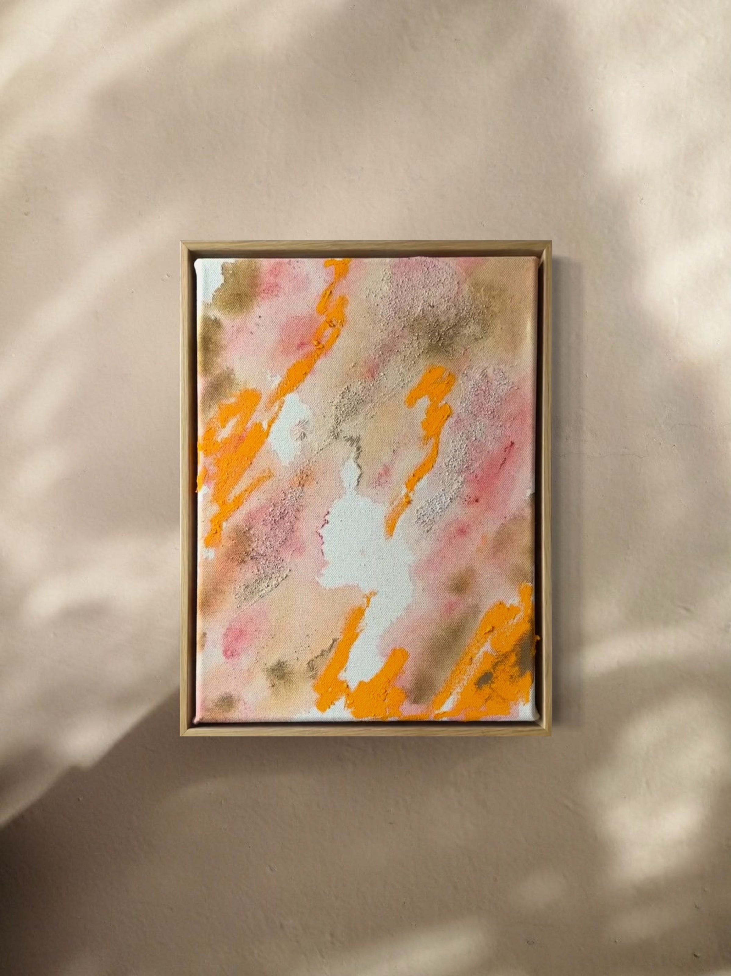 Abstract painting featuring swirling patterns in orange, pink, and beige tones on a textured canvas. Framed in a light wood frame.