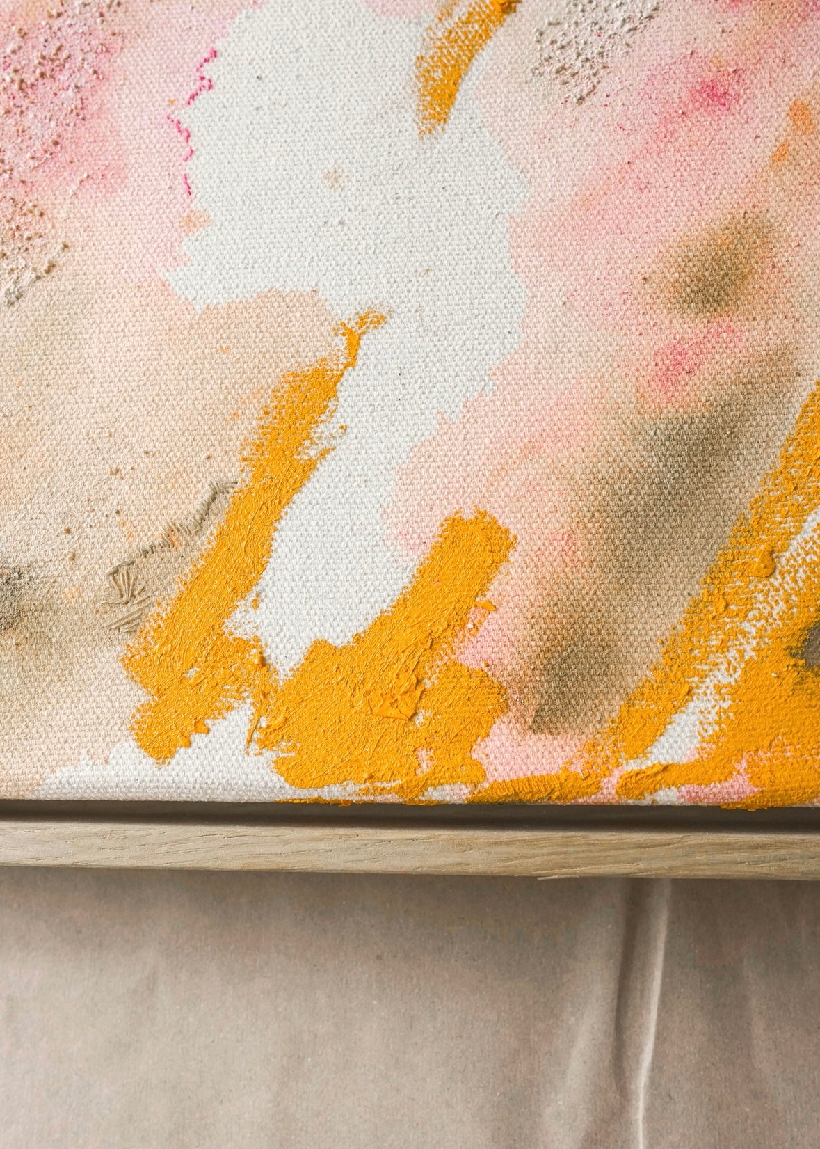 Abstract painting featuring swirling patterns in orange, pink, and beige tones on a textured canvas. Framed in a light wood frame.