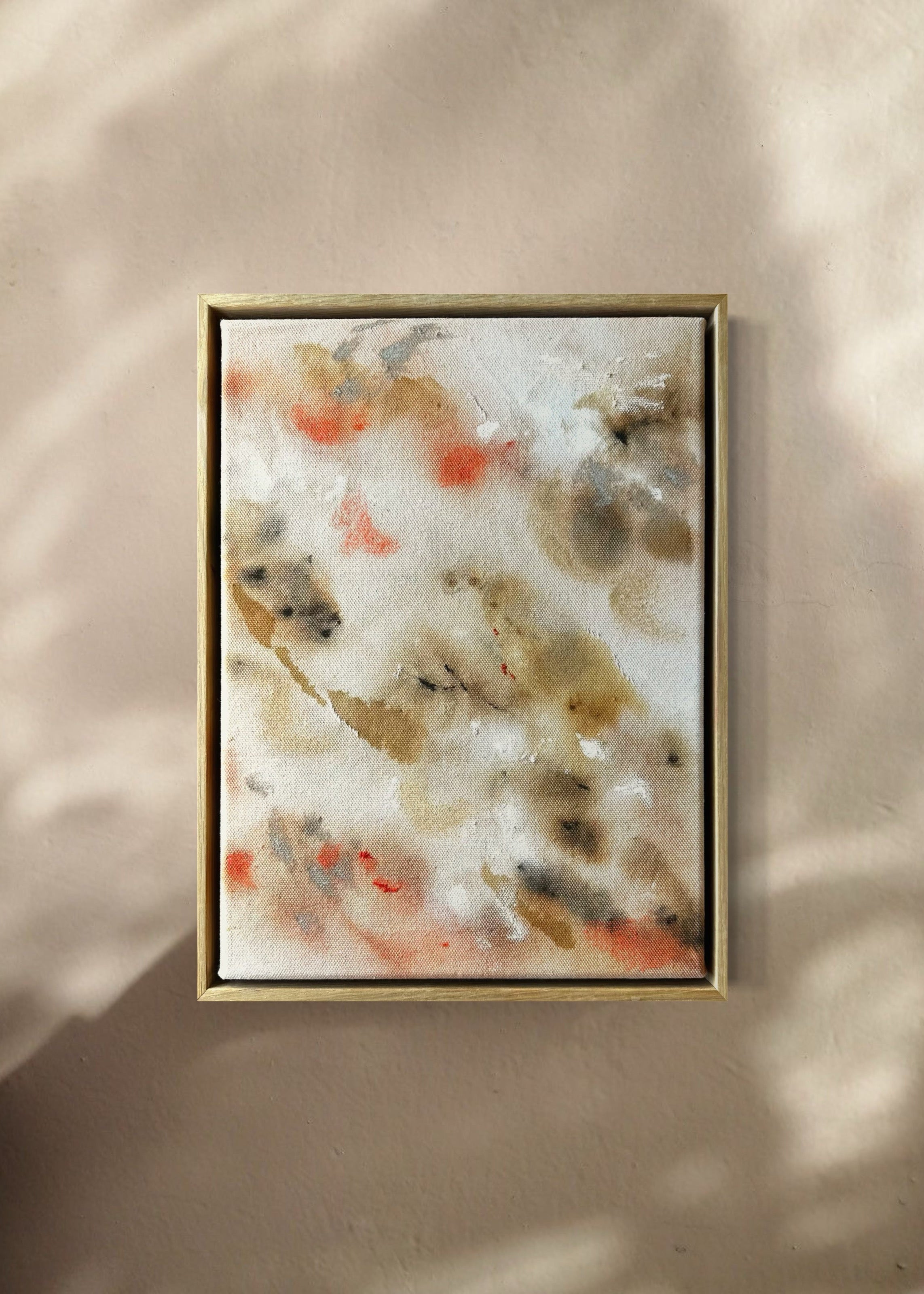 Abstract painting featuring soft, blended shapes in beige, brown, and hints of orange. The artwork has a textured, stitched surface and is framed in a light oak wood frame.