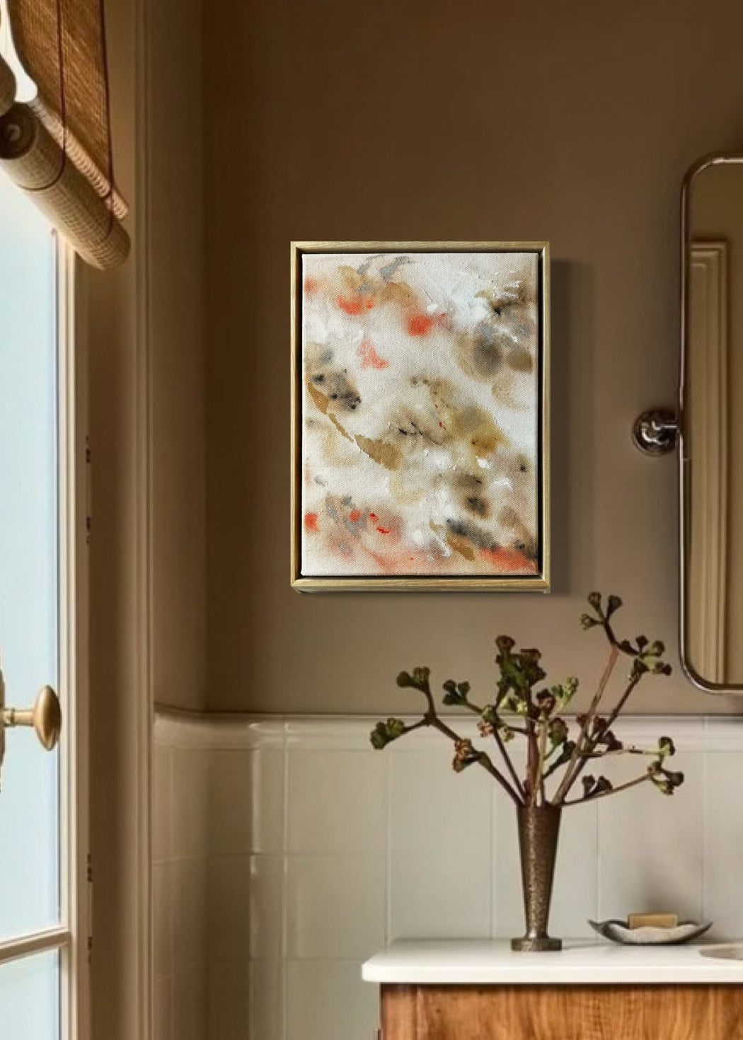 Abstract painting featuring soft, blended shapes in beige, brown, and hints of orange. The artwork has a textured, stitched surface and is framed in a light oak wood frame.