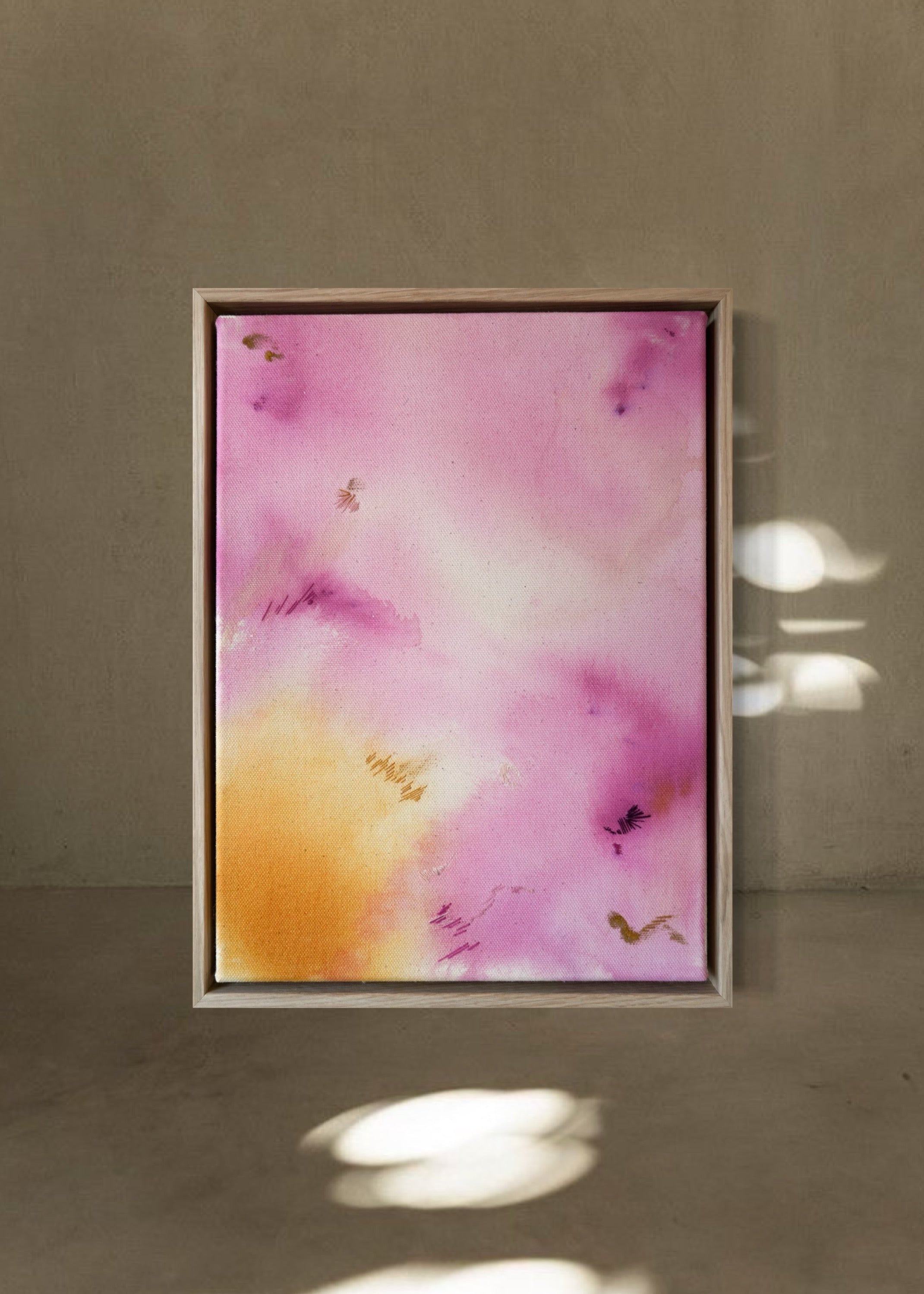 Abstract painting with soft pink, purple, and yellow tones blending across the canvas, accented by small embroideries in pink and yellow, framed in natural wood