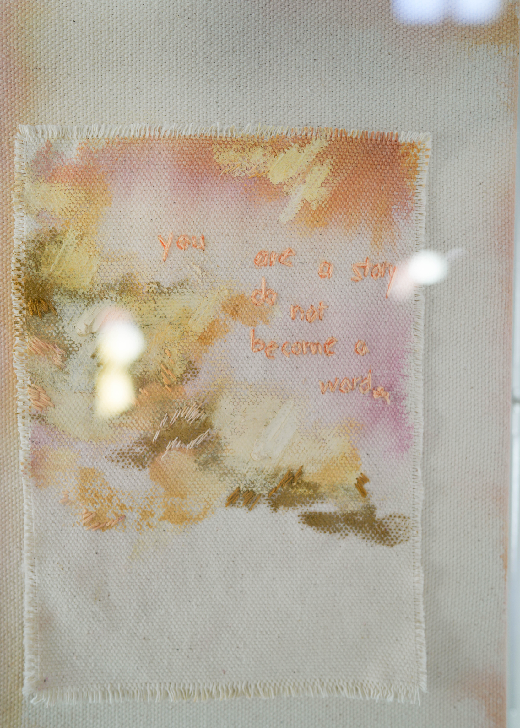 This textured abstract artwork showcases soft pastel shades of pink and orange. It features gentle brushstrokes and embroidered text that reads, "You are a story; do not become a word." The piece is elegantly framed in clear acrylic.
