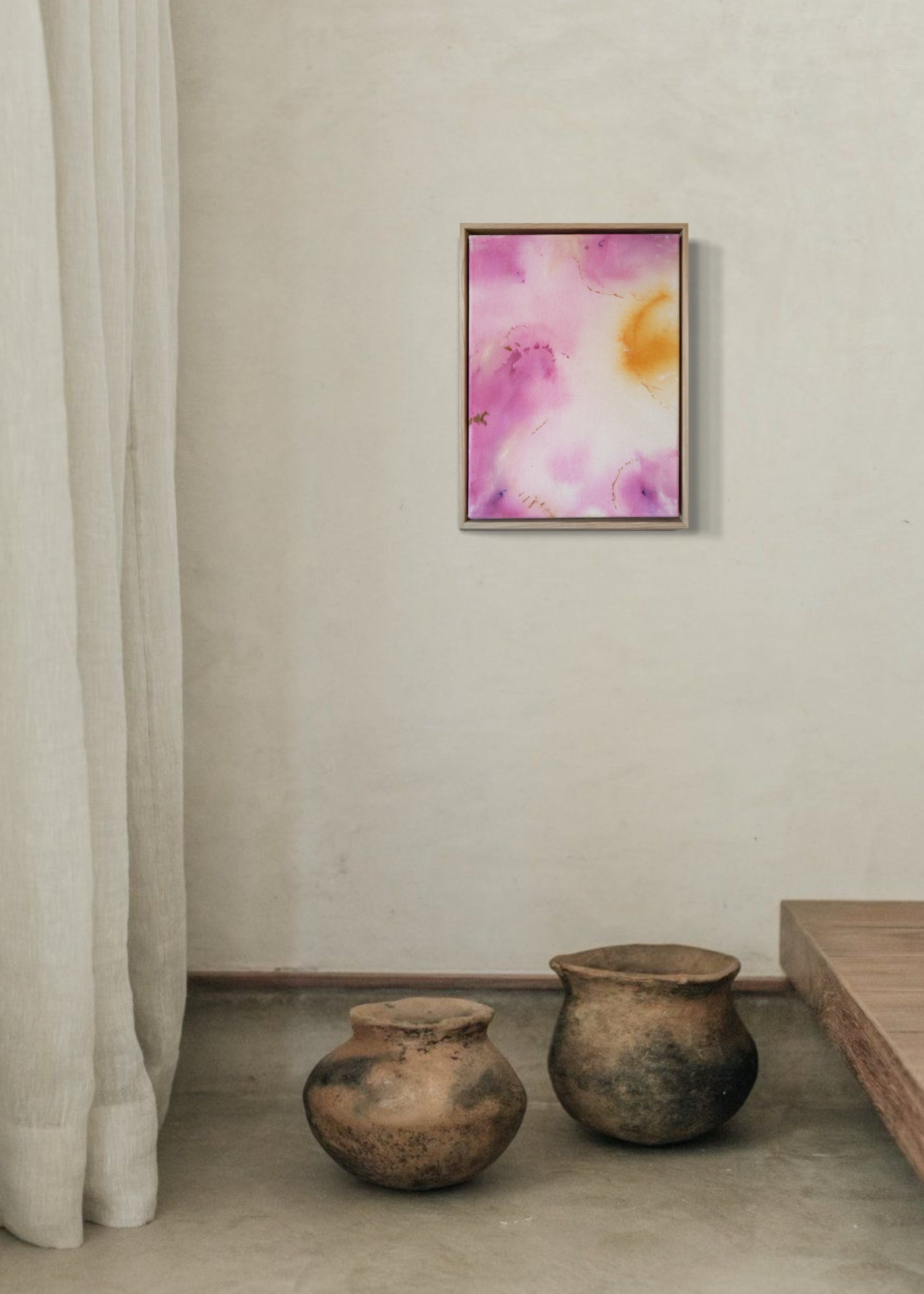 Abstract painting featuring soft pink, purple, and orange hues blending together with embroidery details of gold and dark purple on a canvas, framed in light wood.