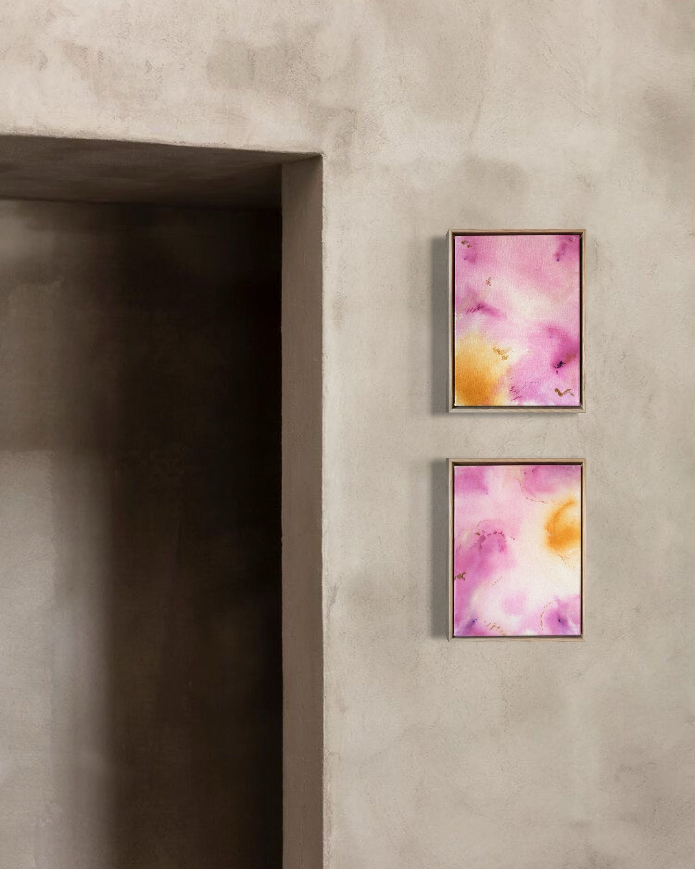 Abstract painting featuring soft pink, purple, and orange hues blending together with embroidery details of gold and dark purple on a canvas, framed in light wood.