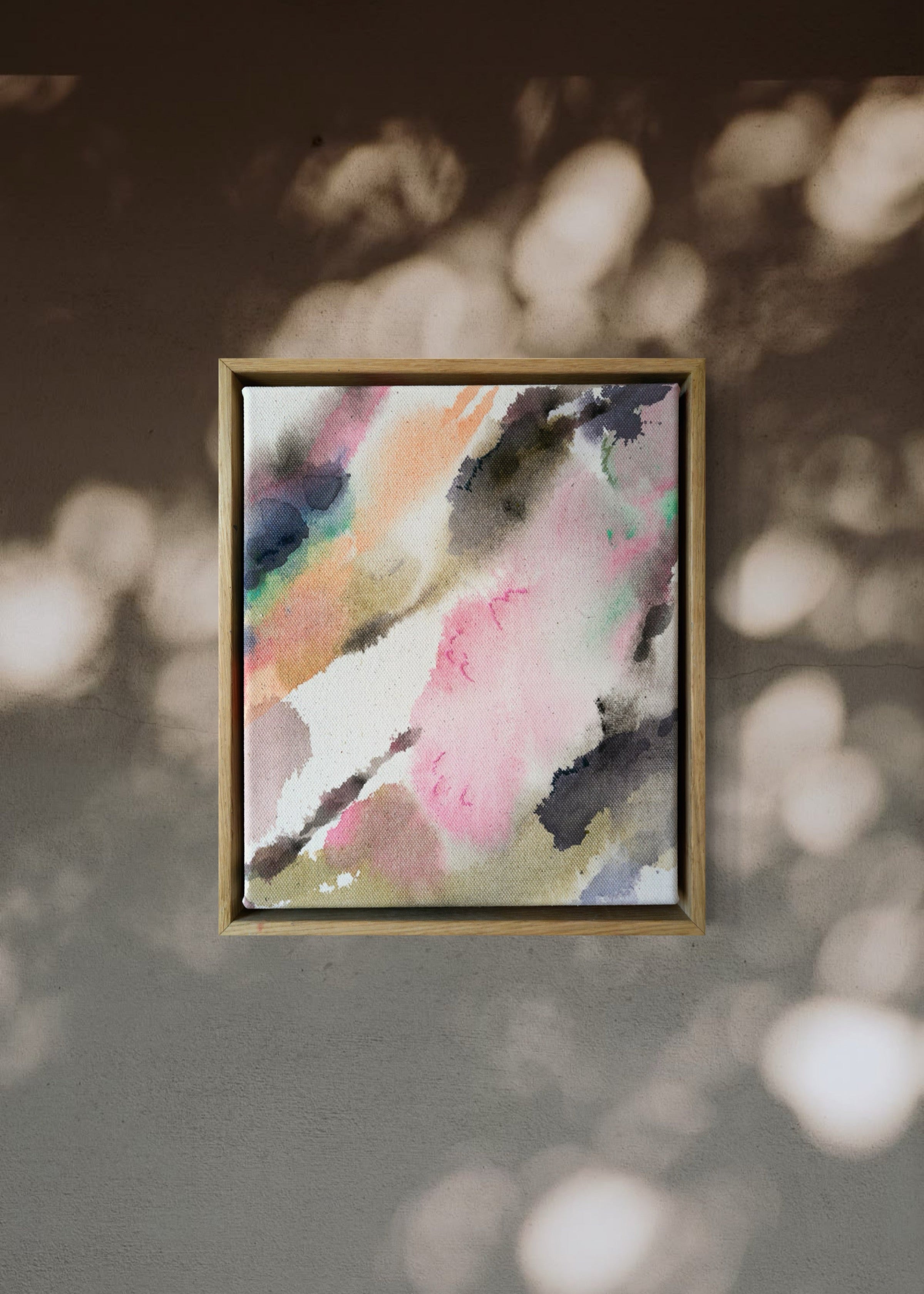 Abstract acrylic, fluid painting with soft pink, peach, green, and dark grey splashes, framed by light wood, conveying an impressionistic and soothing tone.