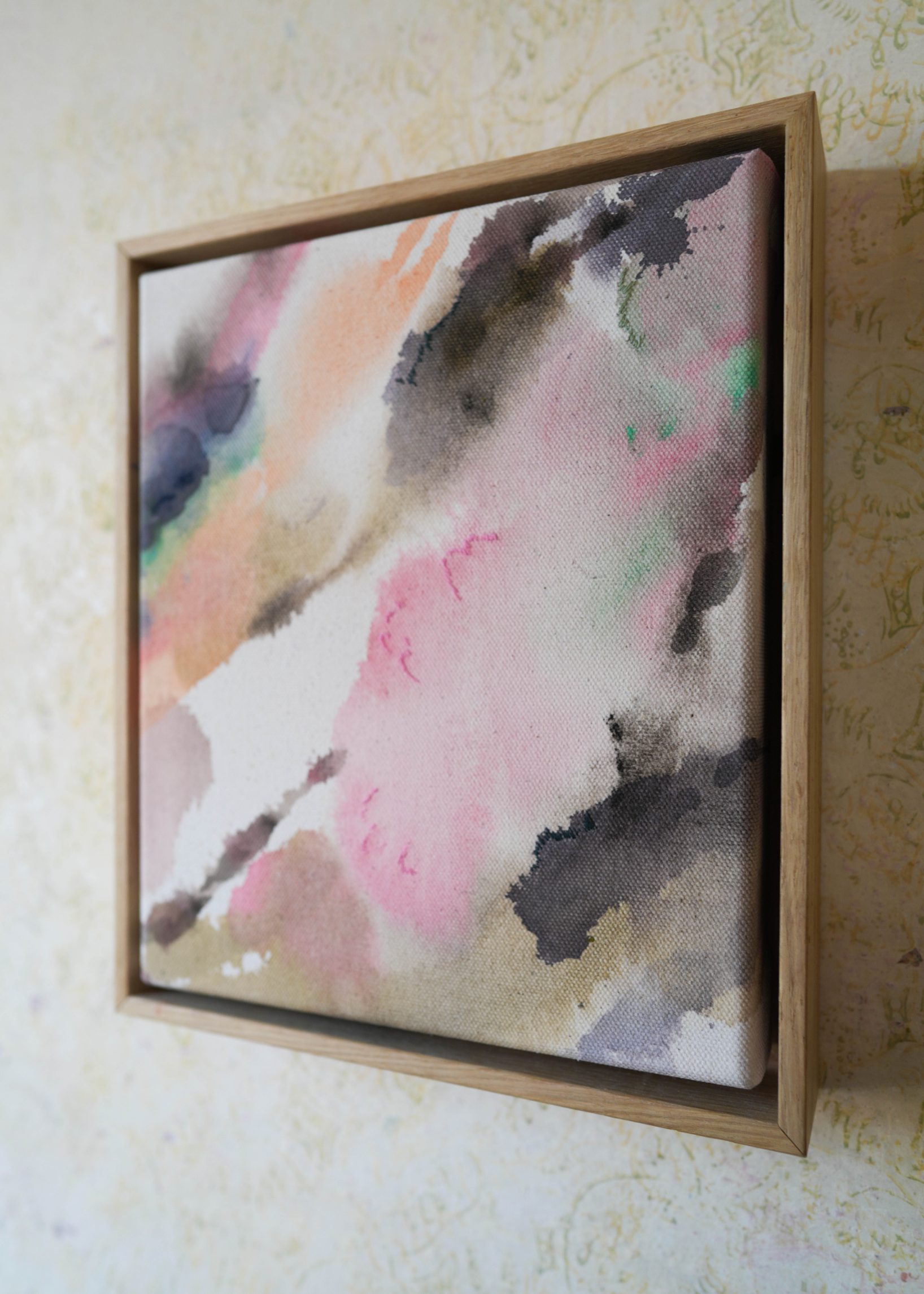 Abstract acrylic, fluid painting with soft pink, peach, green, and dark grey splashes, framed by light wood, conveying an impressionistic and soothing tone.
