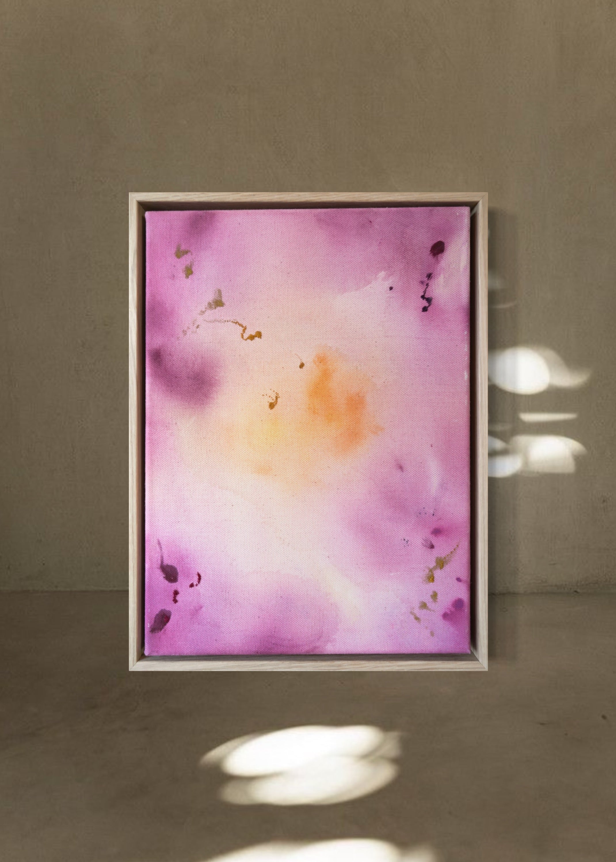 Abstract painting featuring soft pink, purple, and orange hues blending together with embroidery details of gold and dark purple on a canvas, framed in light wood.