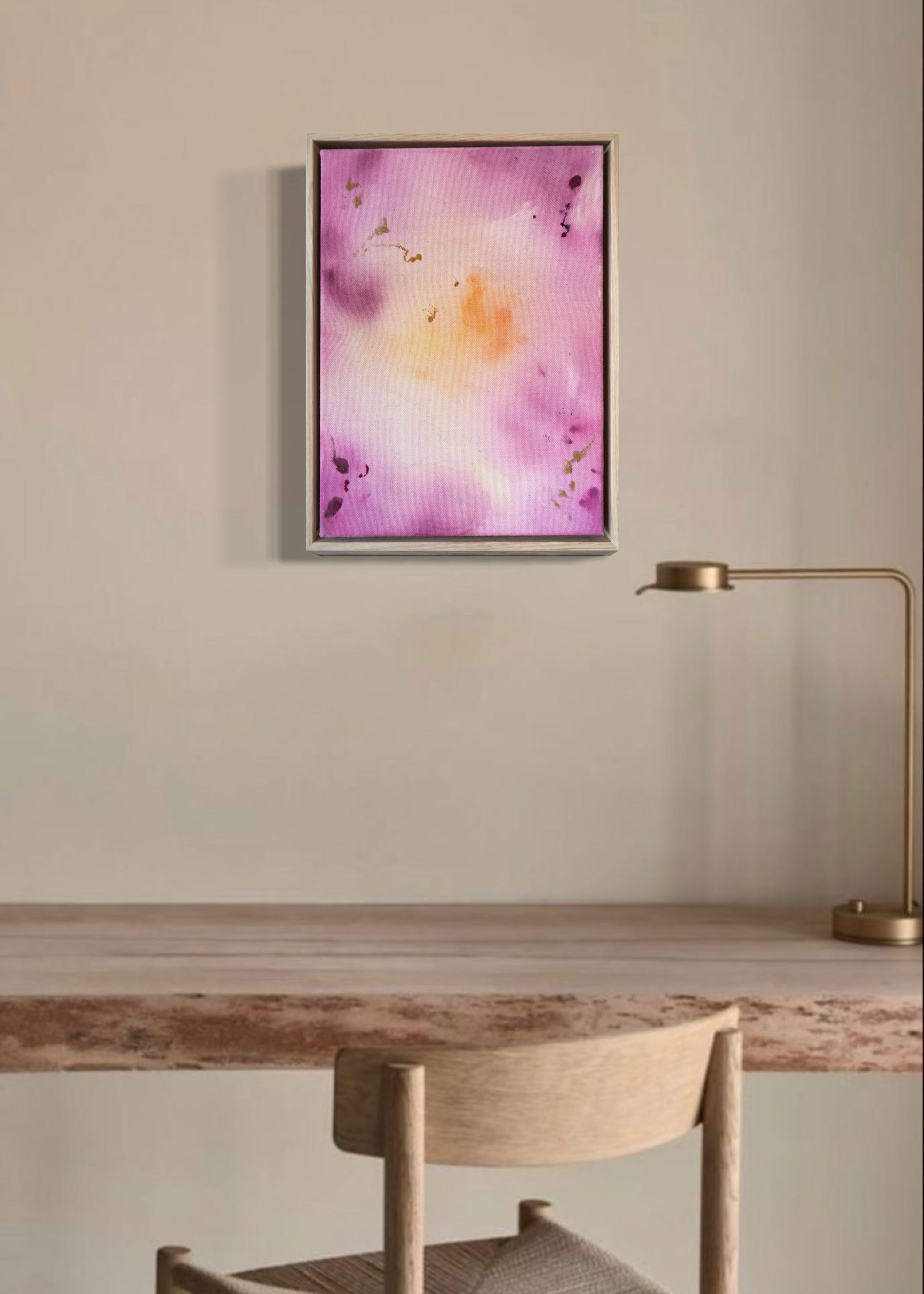 Abstract painting featuring soft pink, purple, and orange hues blending together with embroidery details of gold and dark purple on a canvas, framed in light wood.