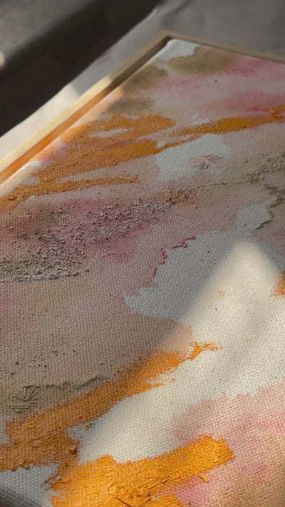 Abstract painting featuring swirling patterns in orange, pink, and beige tones on a textured canvas. Framed in a light wood frame.