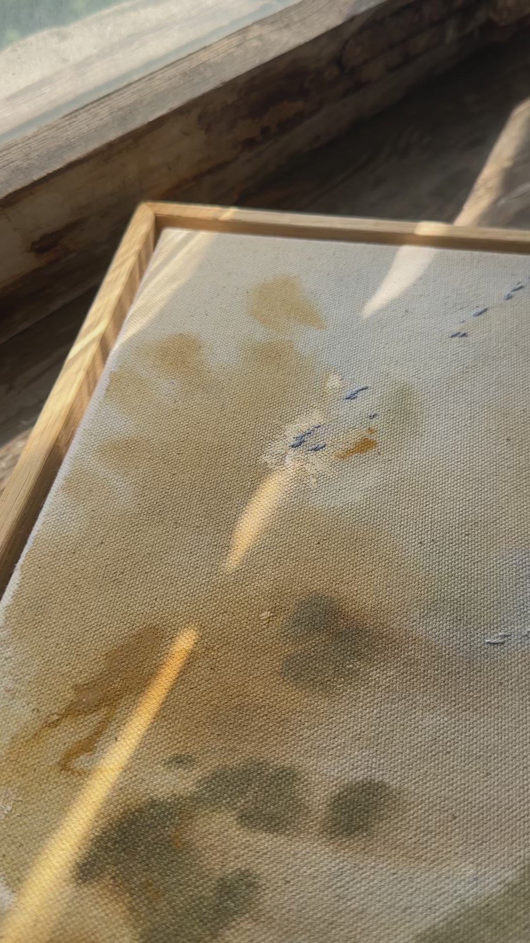 Abstract painting featuring soft, blended colors in beige, brown, and hints of blue. The artwork has a textured, stitched surface and is framed in a light oak wood frame.
